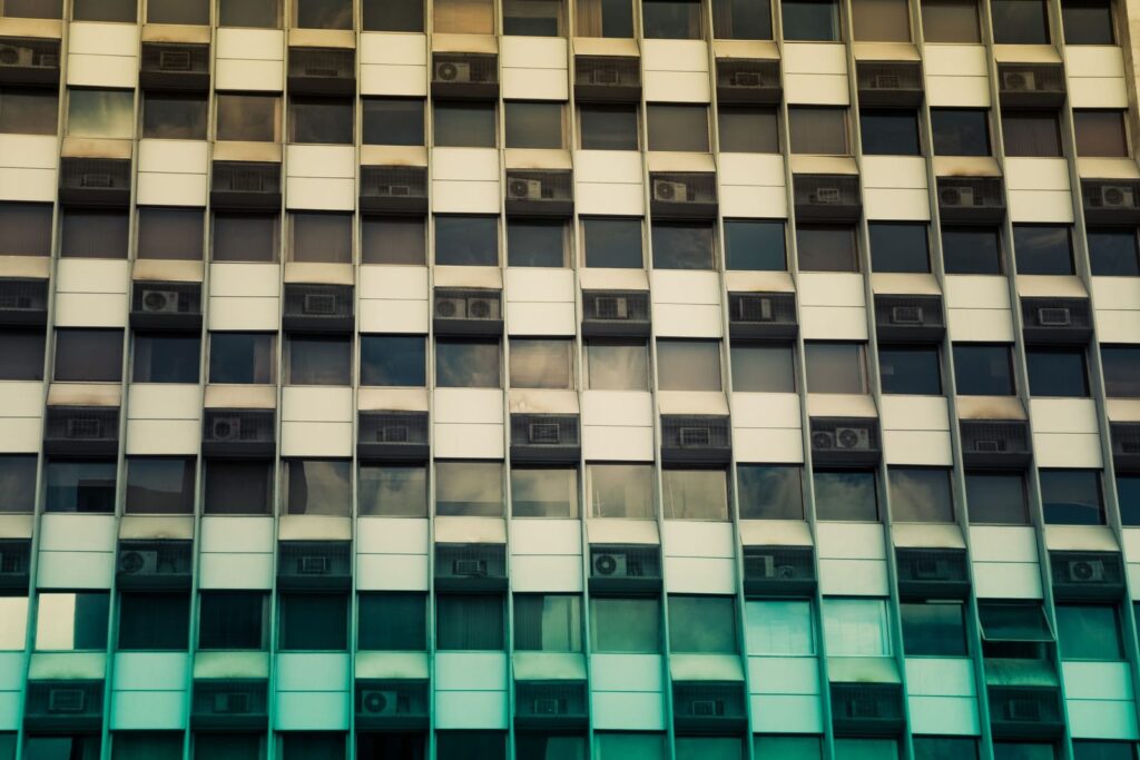 The gridded facade of an older office block with rows of windows and air conditioning units