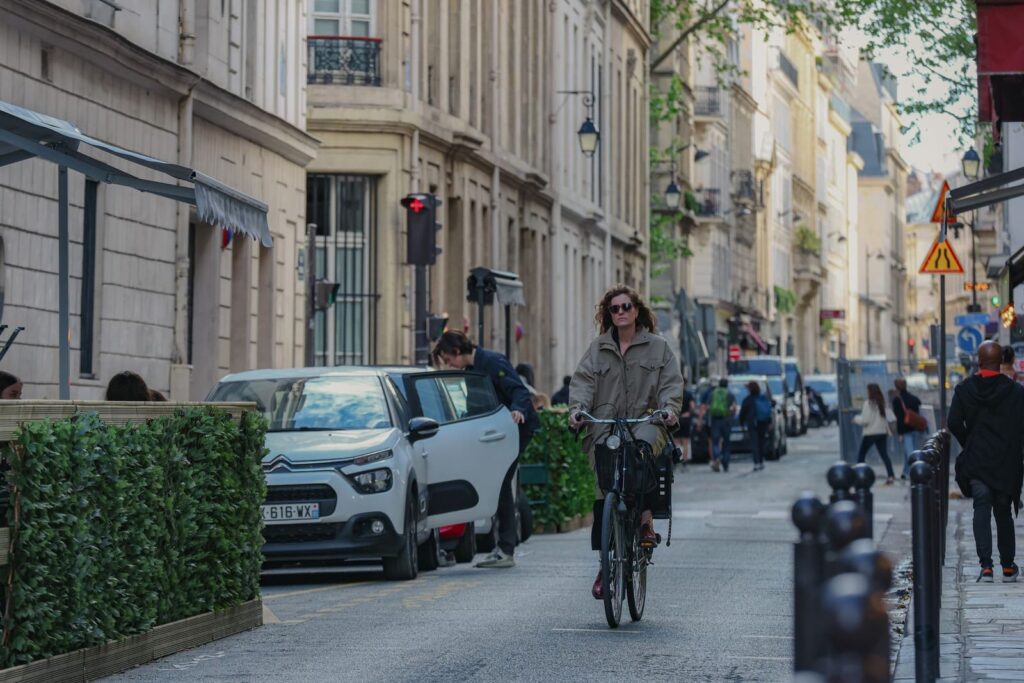 A woman cycling down a Paris side street past cafe terraces and pedestrians